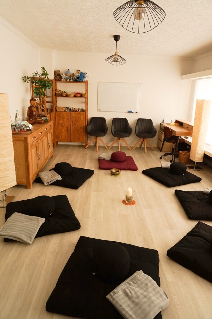 Im Beratungsraum sind Plätze zum meditieren mit Meditationsunterlagen, Kissen und Decken eingerichtet. in der Mitte steht eine Kerze und neben dem Platz des Coaches steht eine Klangschale