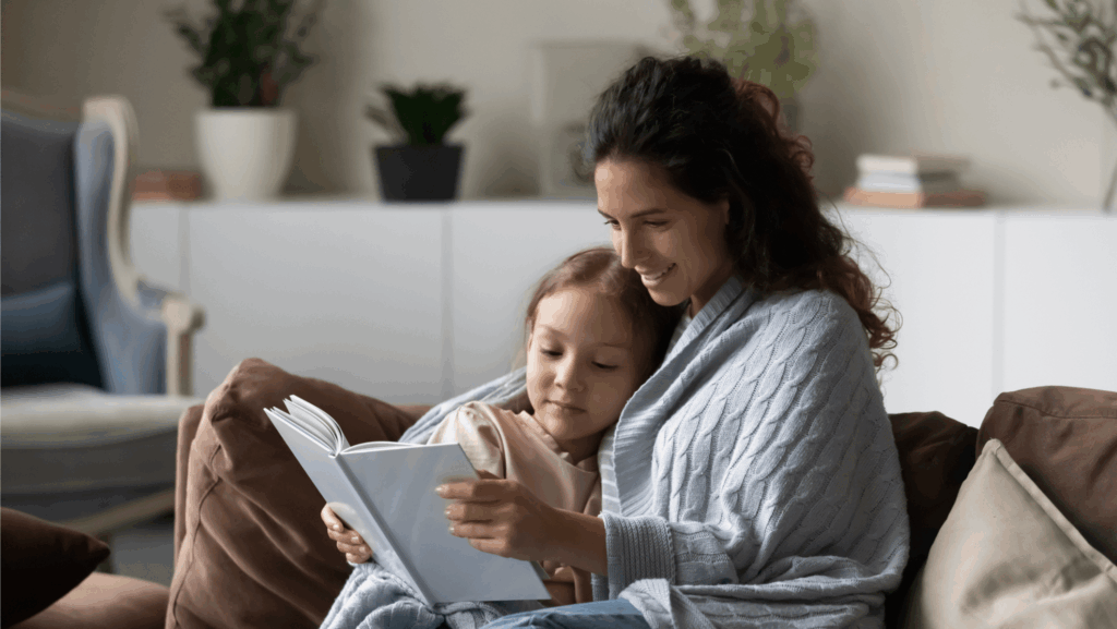 Mutter und Kind sitzen eng beieinander auf dem Sofa und lesen gemeinsam ein Buch – eine ruhige, geborgene Alltagsszene als Symbol für intuitive Begleitung und Co-Regulation.