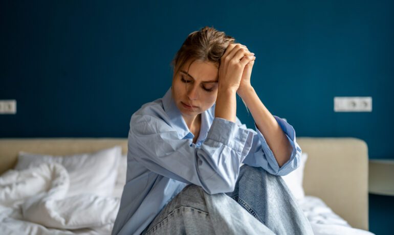 Frau sitzt erschöpft auf dem Bett, Kopf in den Händen gestützt – Sinnbild für Überlastung und inneren Zusammenbruch
